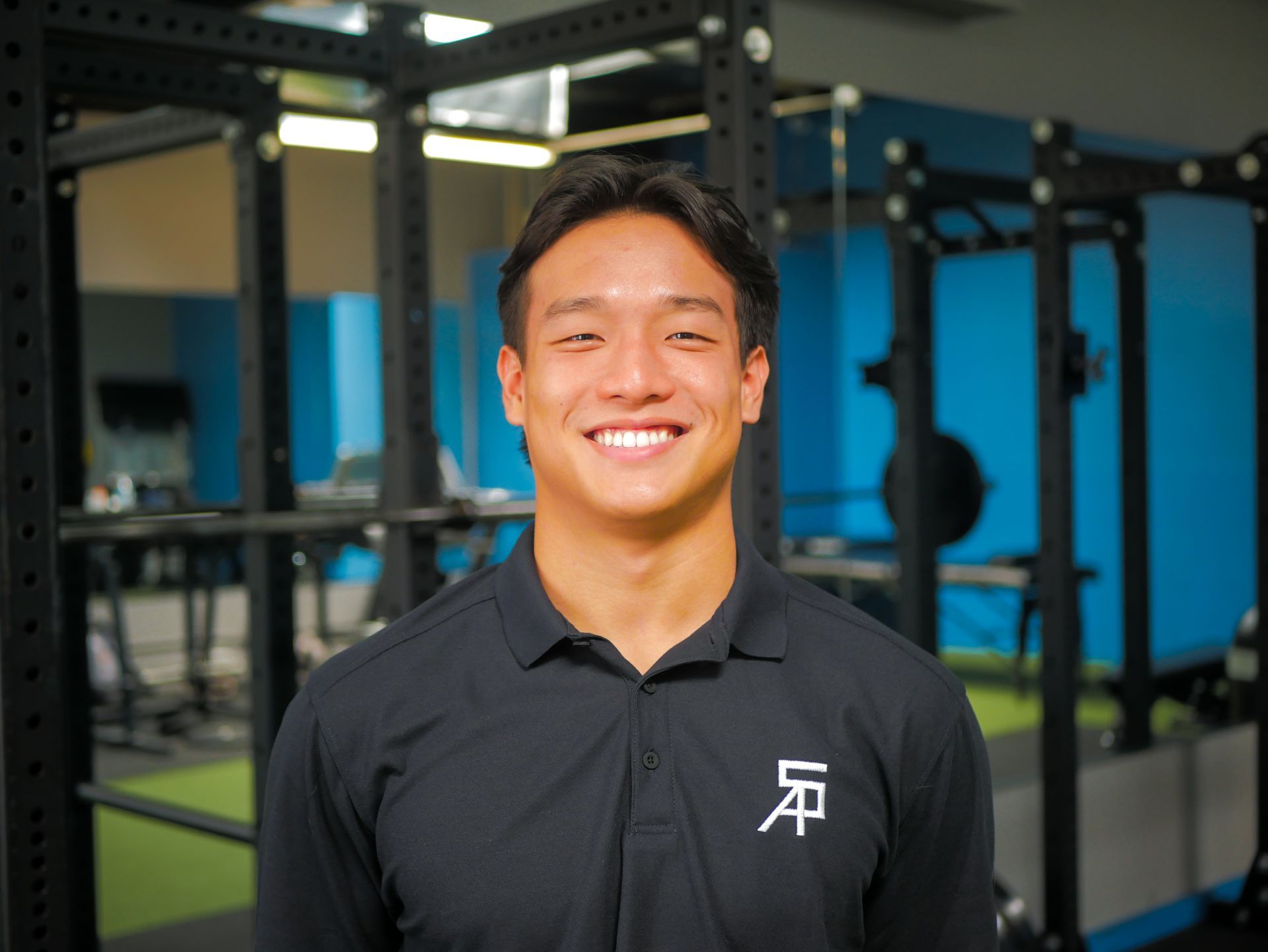 Smiling man in black shirt in a gym with workout equipment.