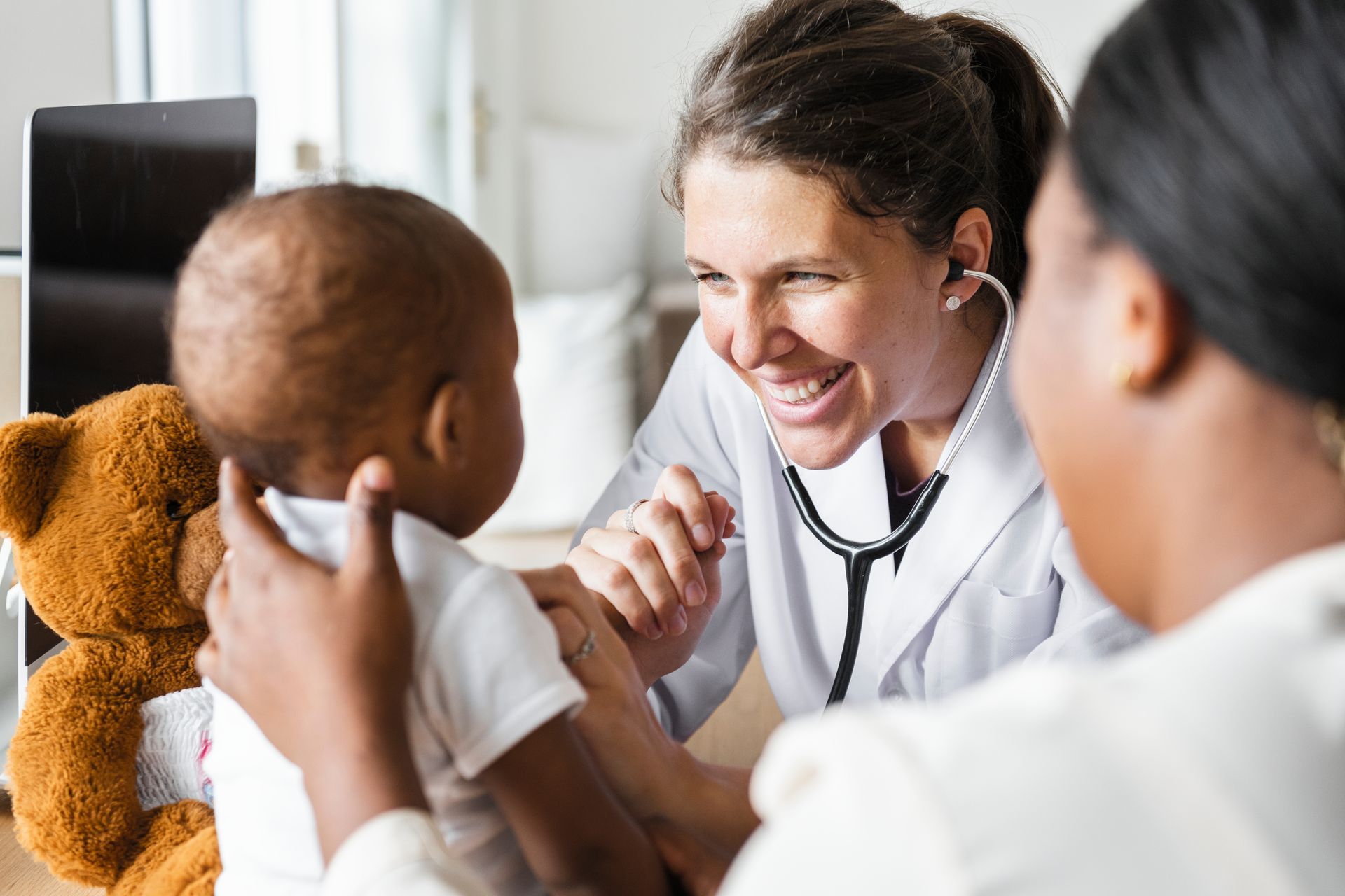 Clinician using a stethoscope to examine an infant held by a caregiver during a pediatric checkup.
