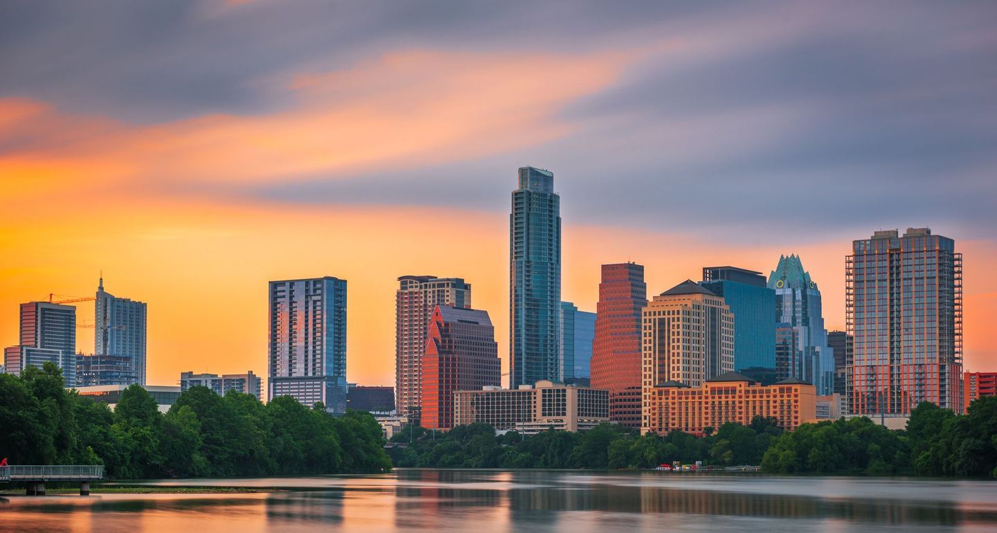 A city skyline with a lake in the foreground at sunset.