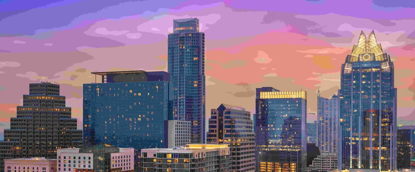 A city skyline at night with a sunset in the background.