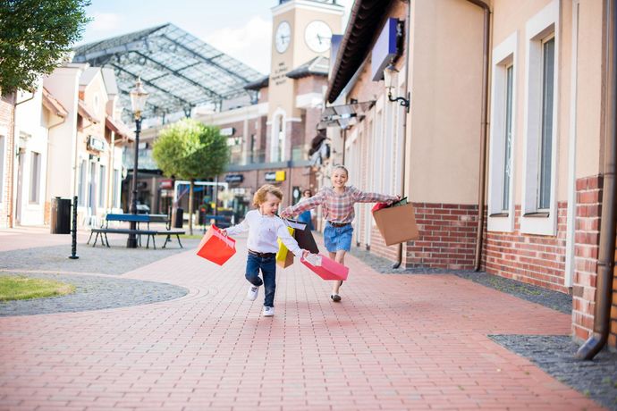 Two children are running down a sidewalk holding shopping bags.