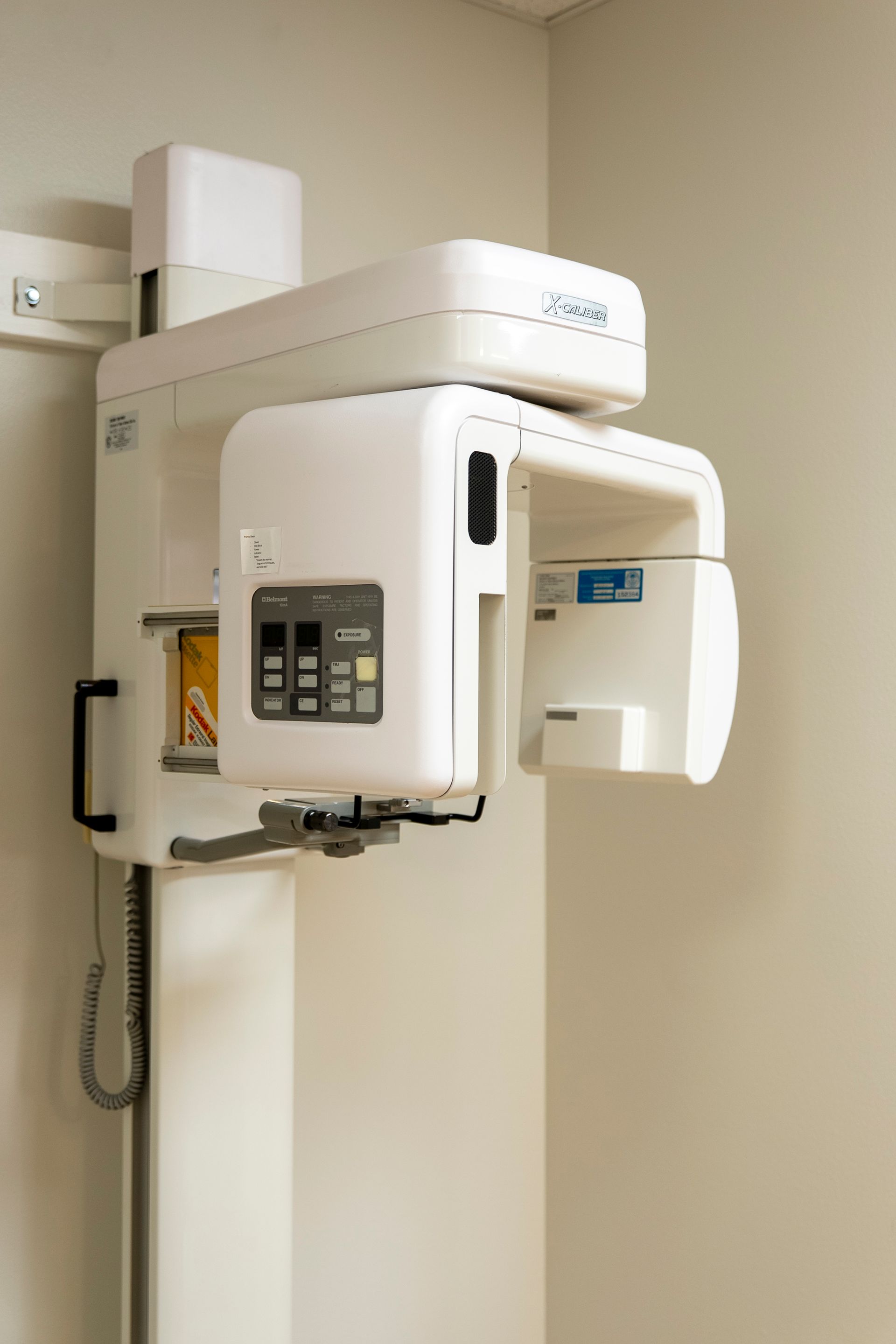 A dental panoramic X-ray machine in a small room with tan walls and dark carpet.