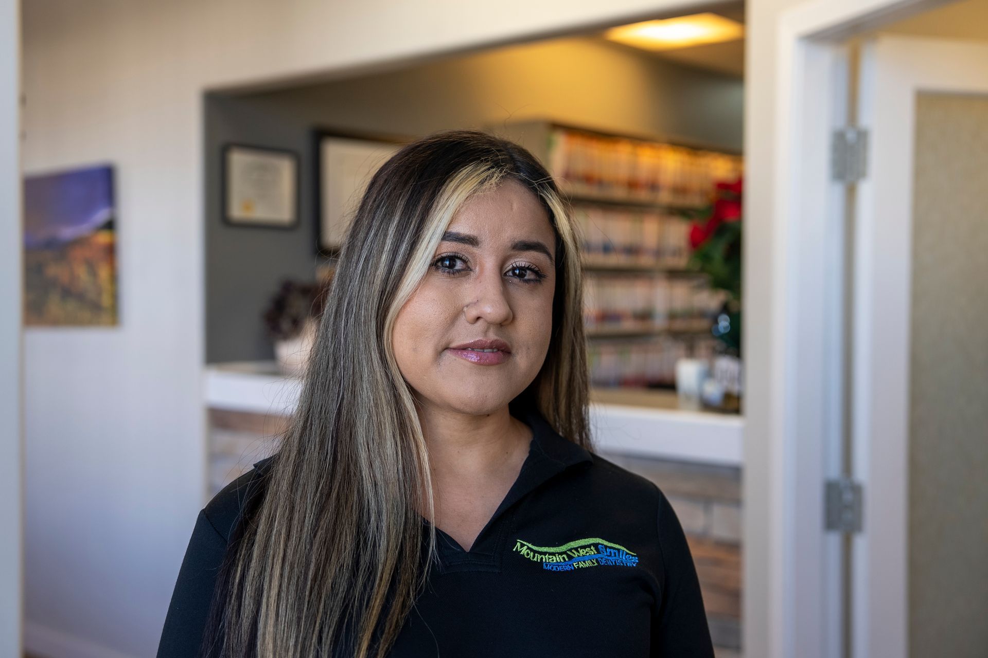 Woman with light brown hair smiles, arms crossed, leaning on counter in a clinic setting.
