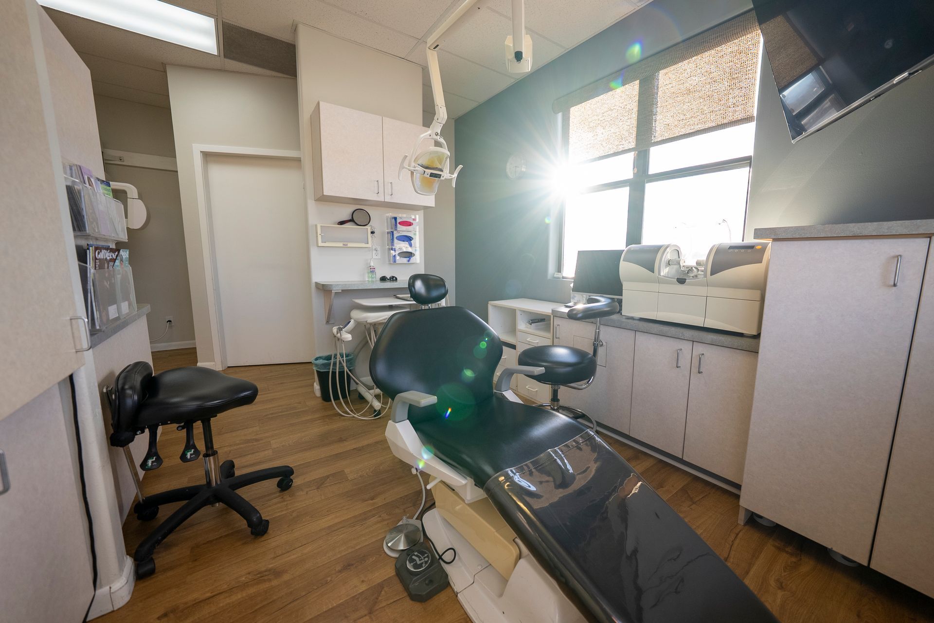 Dental examination room with teal chair, instruments, and beige cabinets.