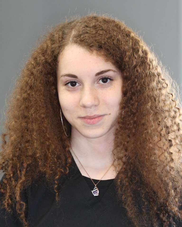 Woman with curly brown hair, wearing a black shirt and silver necklace, looking at the camera.