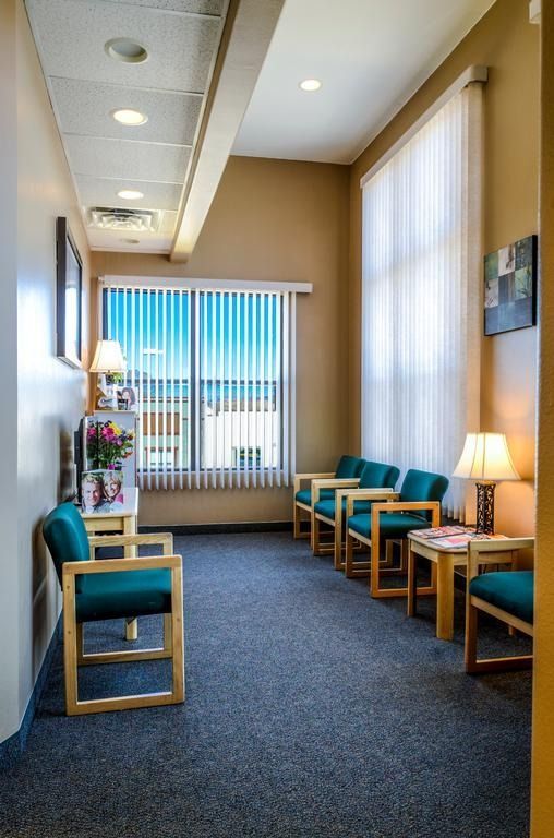 Waiting room with teal chairs, window with blinds, and neutral-colored walls.