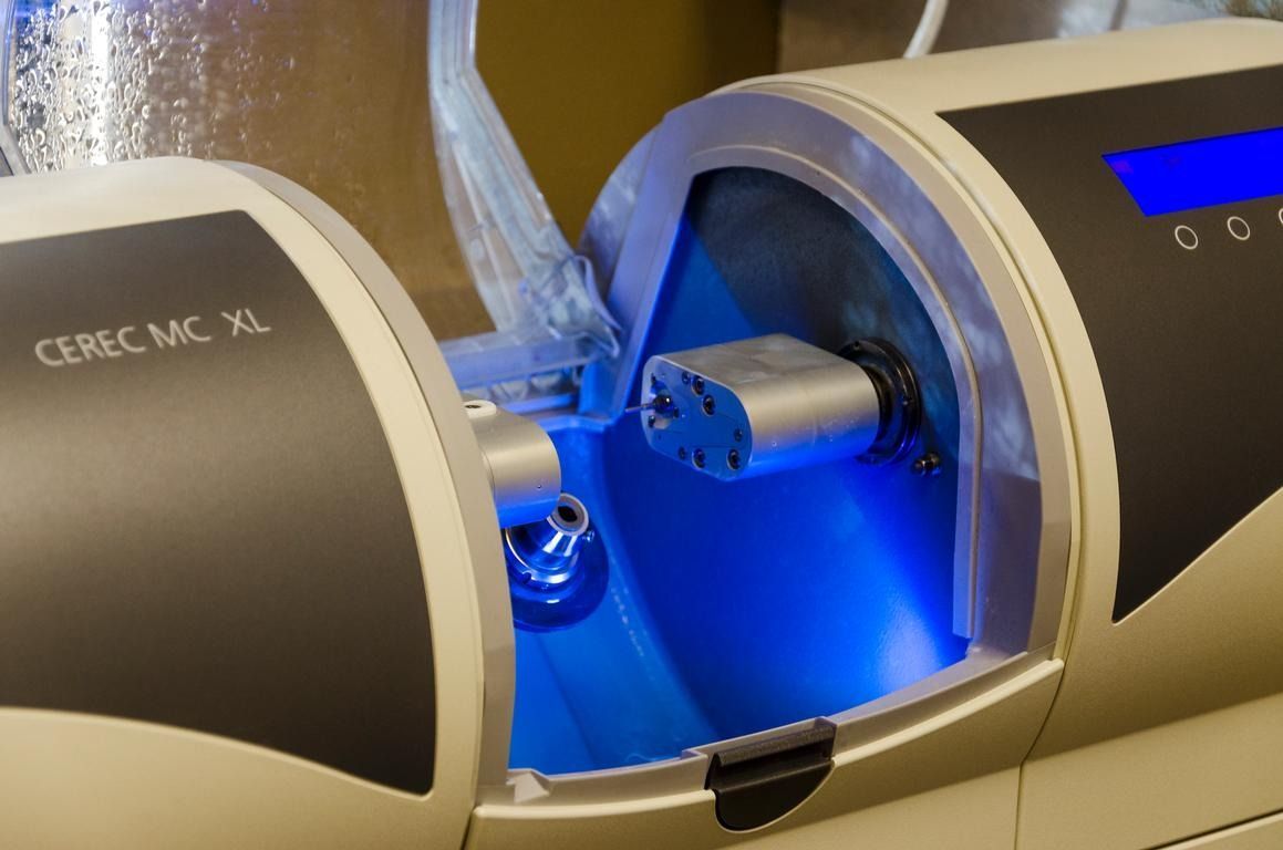 Dental milling machine, CEREC MC XL, in operation with blue light illuminating the interior.