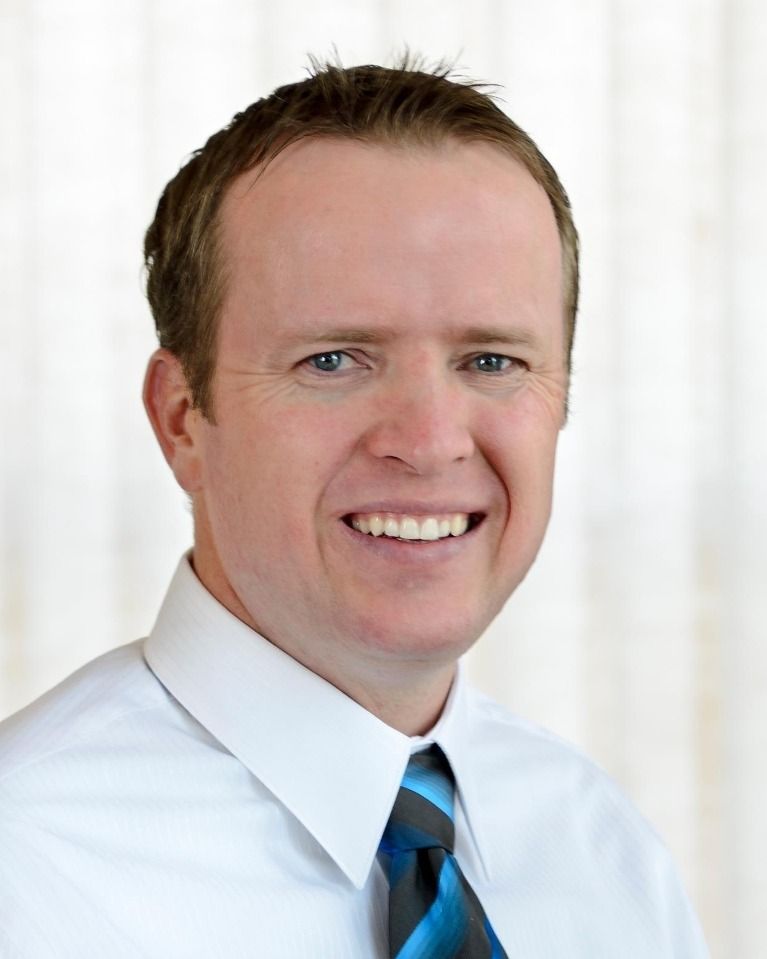 Man in a white shirt and blue striped tie smiles, looking towards the viewer.