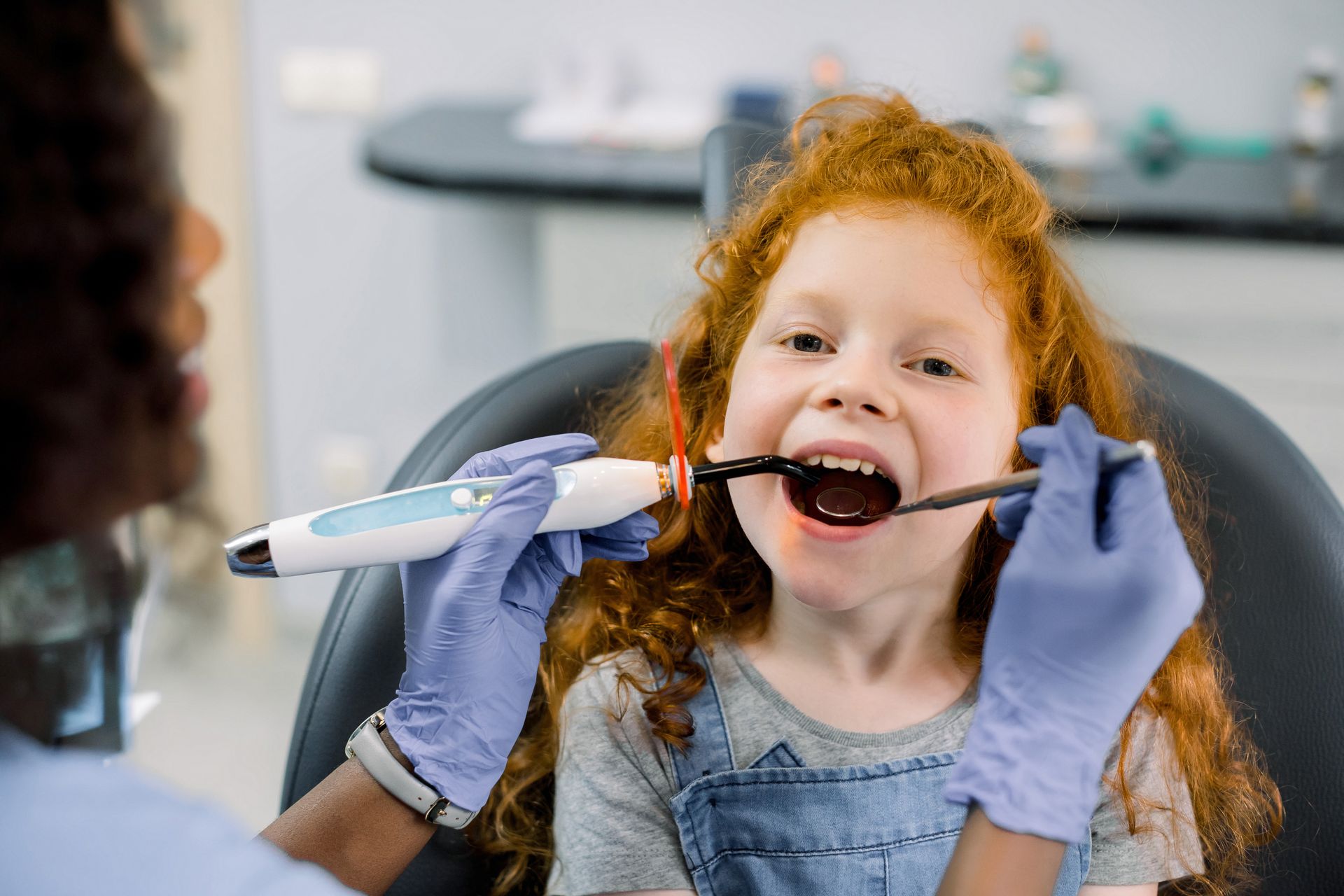 Dentist treating a child's tooth with curing light. Child has mouth open in dental chair.