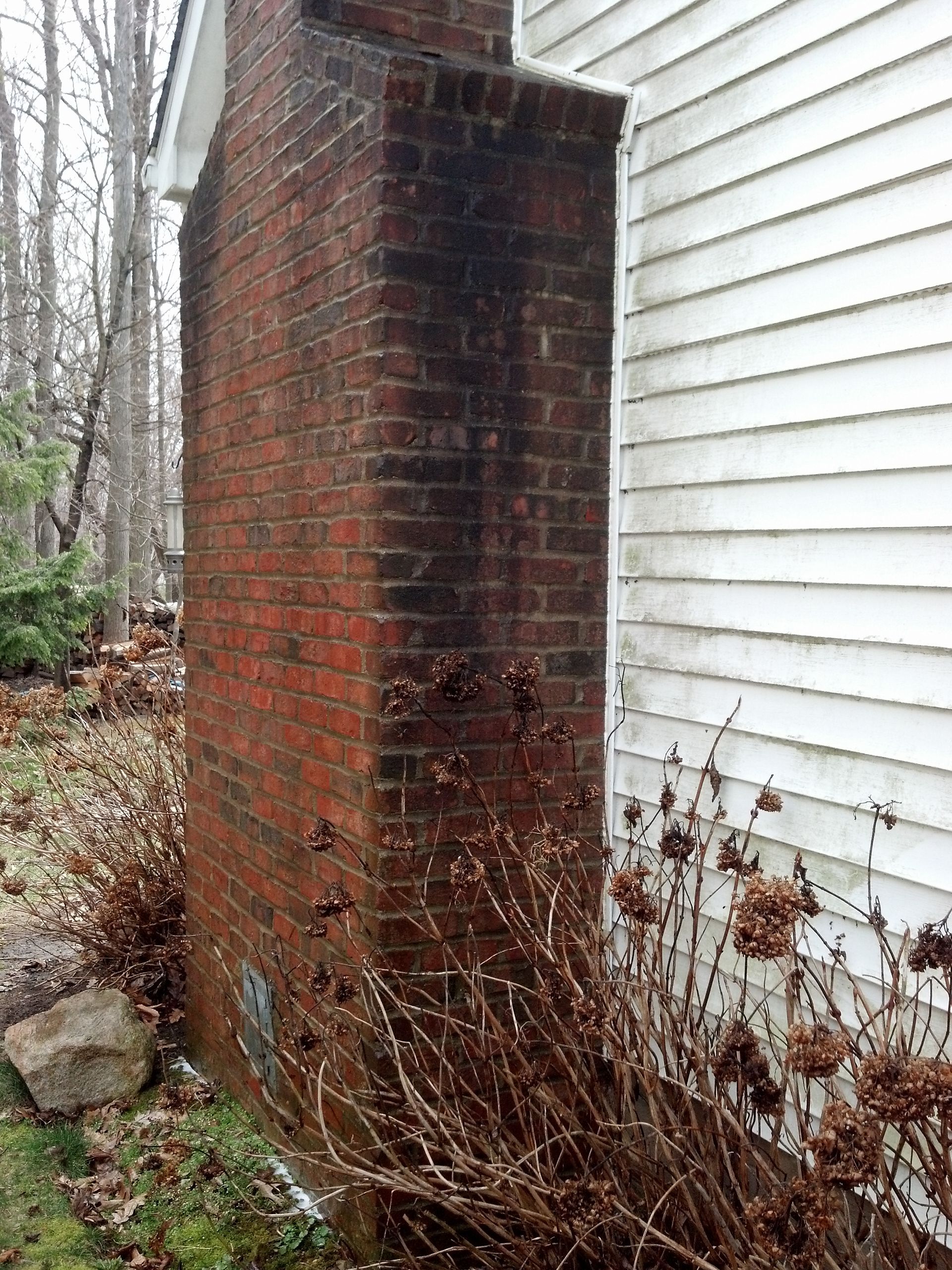 A brick chimney is sitting next to a white house.