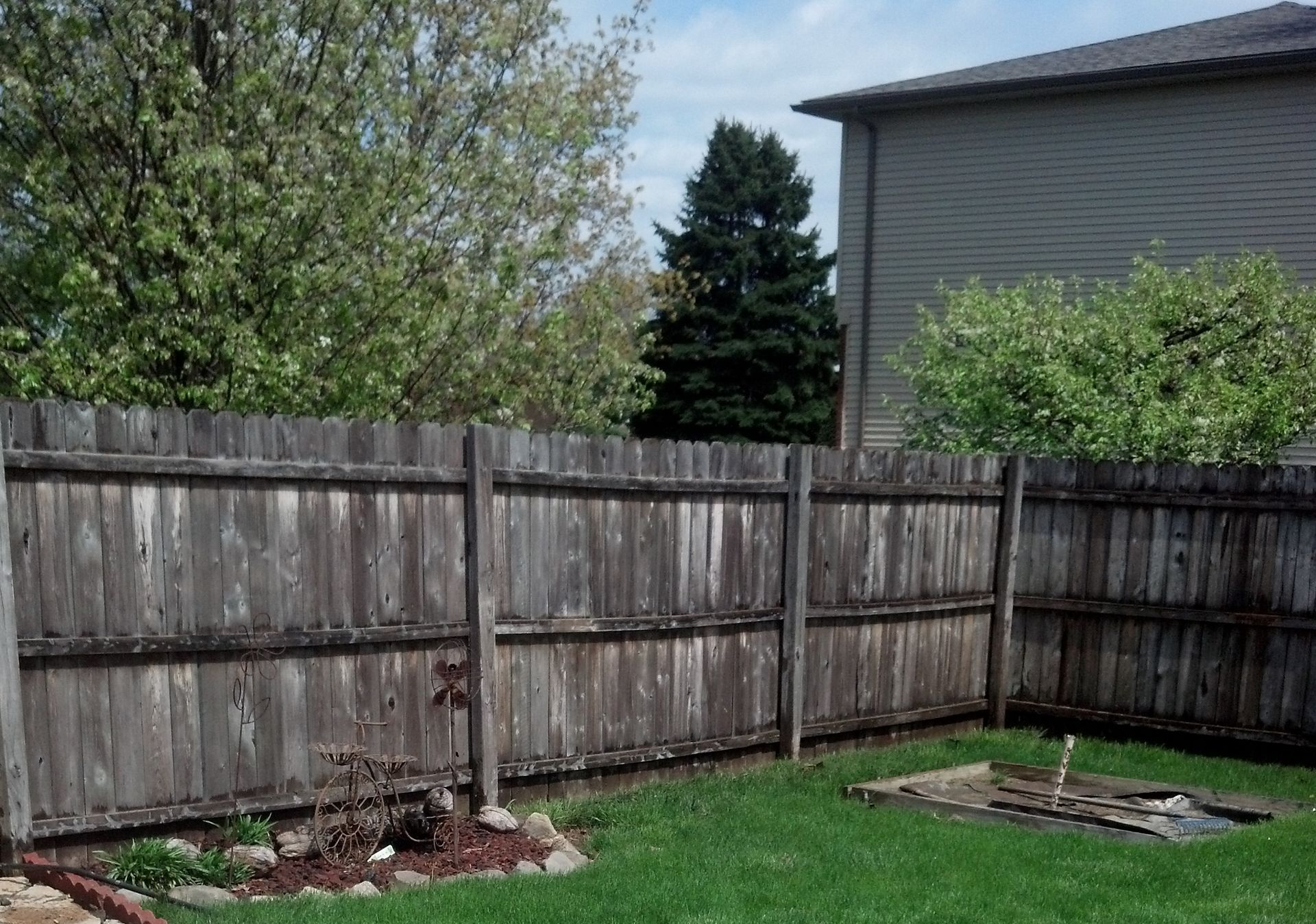 A backyard with a wooden fence and a house in the background before clean