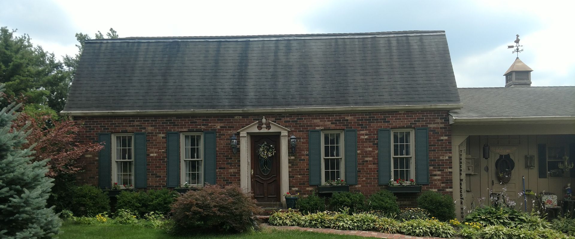 A brick house with a black roof and blue shutters before clean.