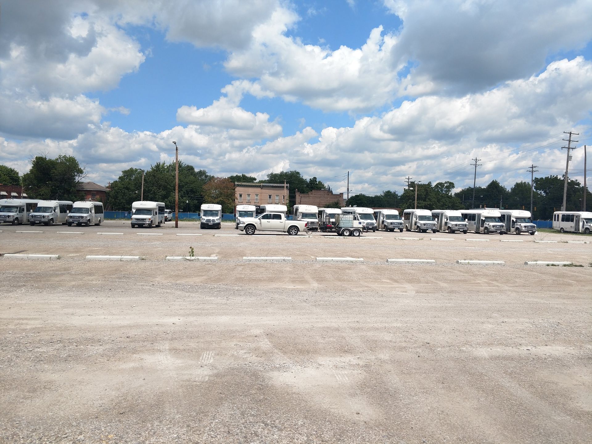 A row of white vans are parked in a gravel lot