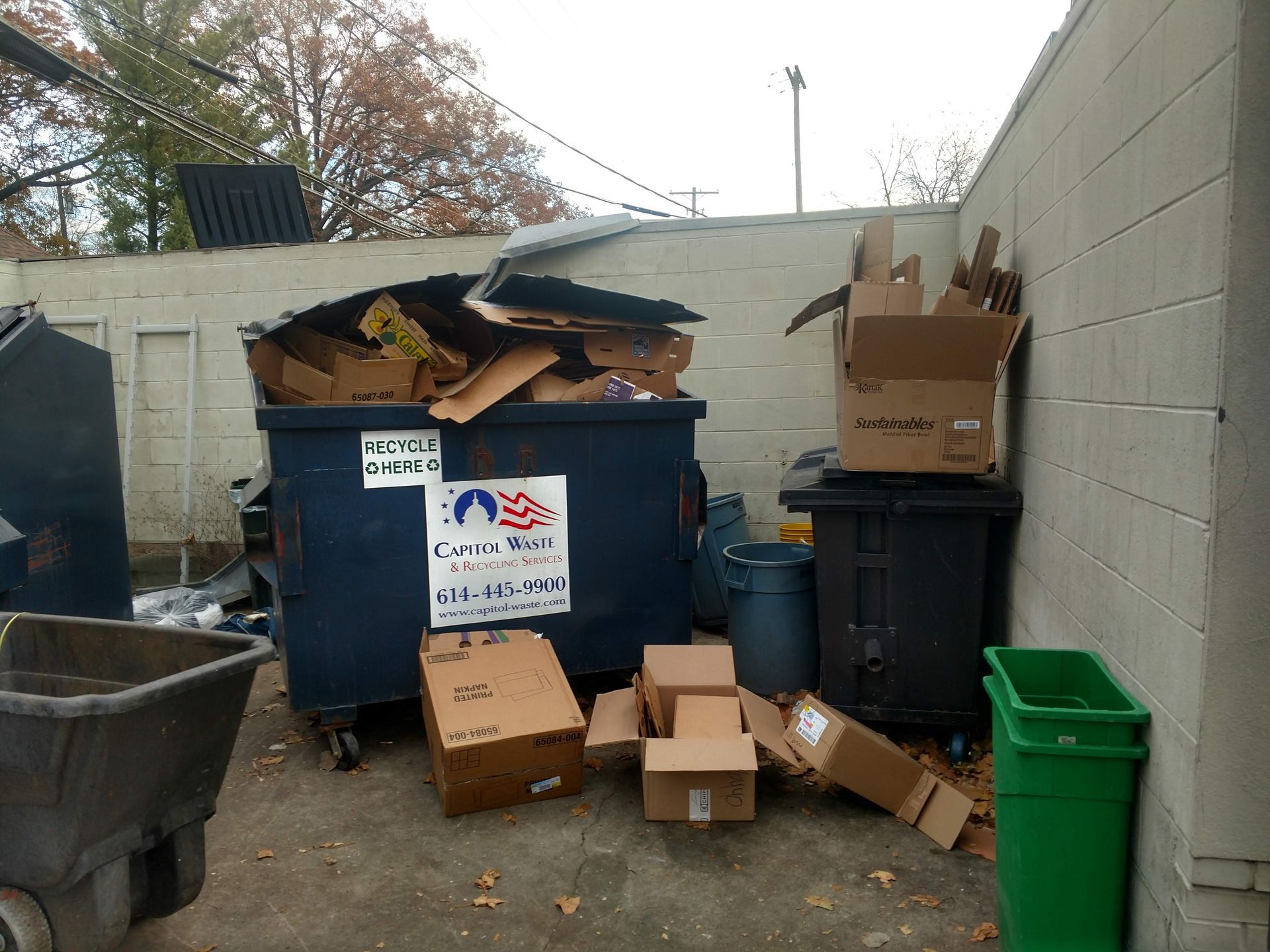 A dumpster filled with cardboard boxes and a sign that says recycle cardboard