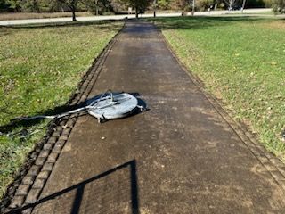 A lawn mower is sitting on the side of a path in a park before clean.