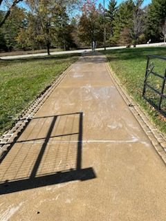 A shadow of a fence is cast on a concrete walkway in a park after clean.