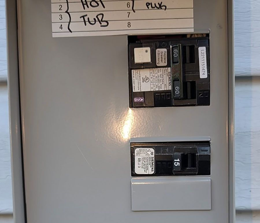 An open gray electrical breaker box mounted on siding, containing a double-pole 50-amp GFCI breaker and a 15-amp breaker.