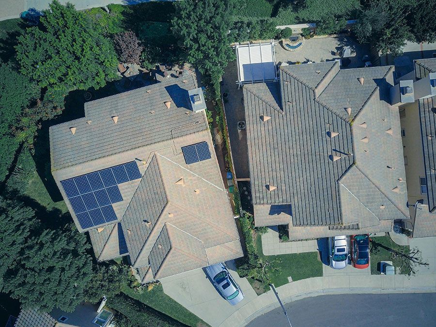 Aerial view of two suburban homes with tiled roofs, one featuring a large solar panel array, near a curved street.