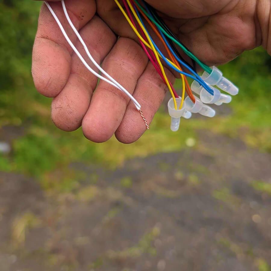A hand holding a wire harness with several multi-colored wires, each tipped with a small, clear plastic connector.