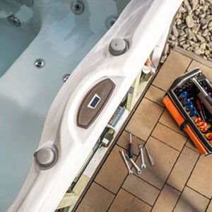 A hot tub control panel edge sits on a patio next to an open toolbox and scattered metal wrenches.