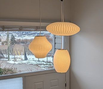 Three off-white, ribbed pendant lights of varying shapes hanging near a window with a snowy landscape view.