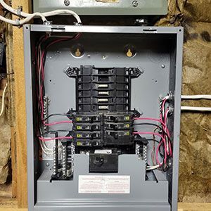An open electrical breaker panel with multiple circuit breakers and wiring installed, mounted on a wooden frame wall.