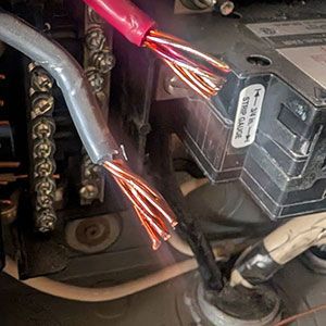 Two exposed, stranded copper electrical wires, one red and one grey, positioned near an electrical terminal block and panel.