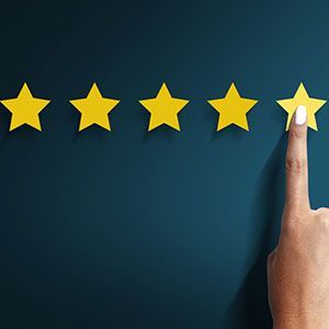 A hand reaching up to touch the fifth yellow star in a row of five on a dark blue background.