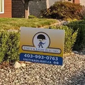 A professional yard sign for Unity & Light Electric with contact information, placed in a garden landscape.