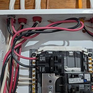 Interior view of an electrical subpanel showing circuit breakers connected to various red, black, and white wiring.