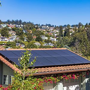 A solar panel array installed on a Spanish-style tile roof, overlooking a hilly residential neighborhood.