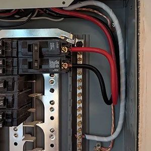 A red wire and a black wire are connected to a double-pole circuit breaker inside a grey electrical panel.