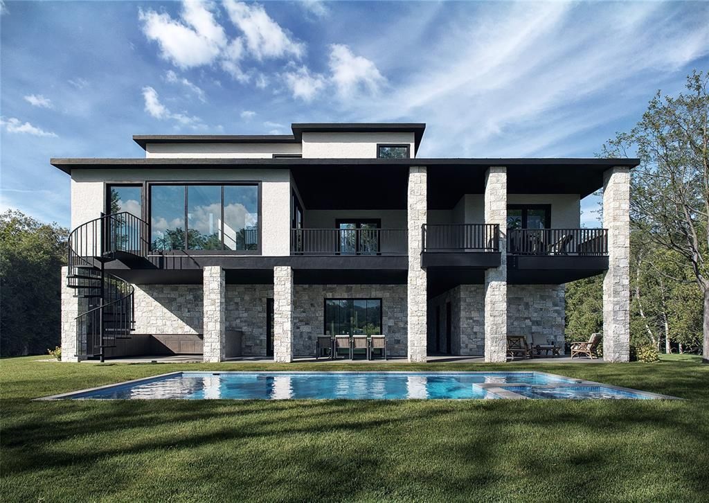 Modern two-story house with stone pillars, balconies, and a pool; set in a grassy yard under a cloudy sky.