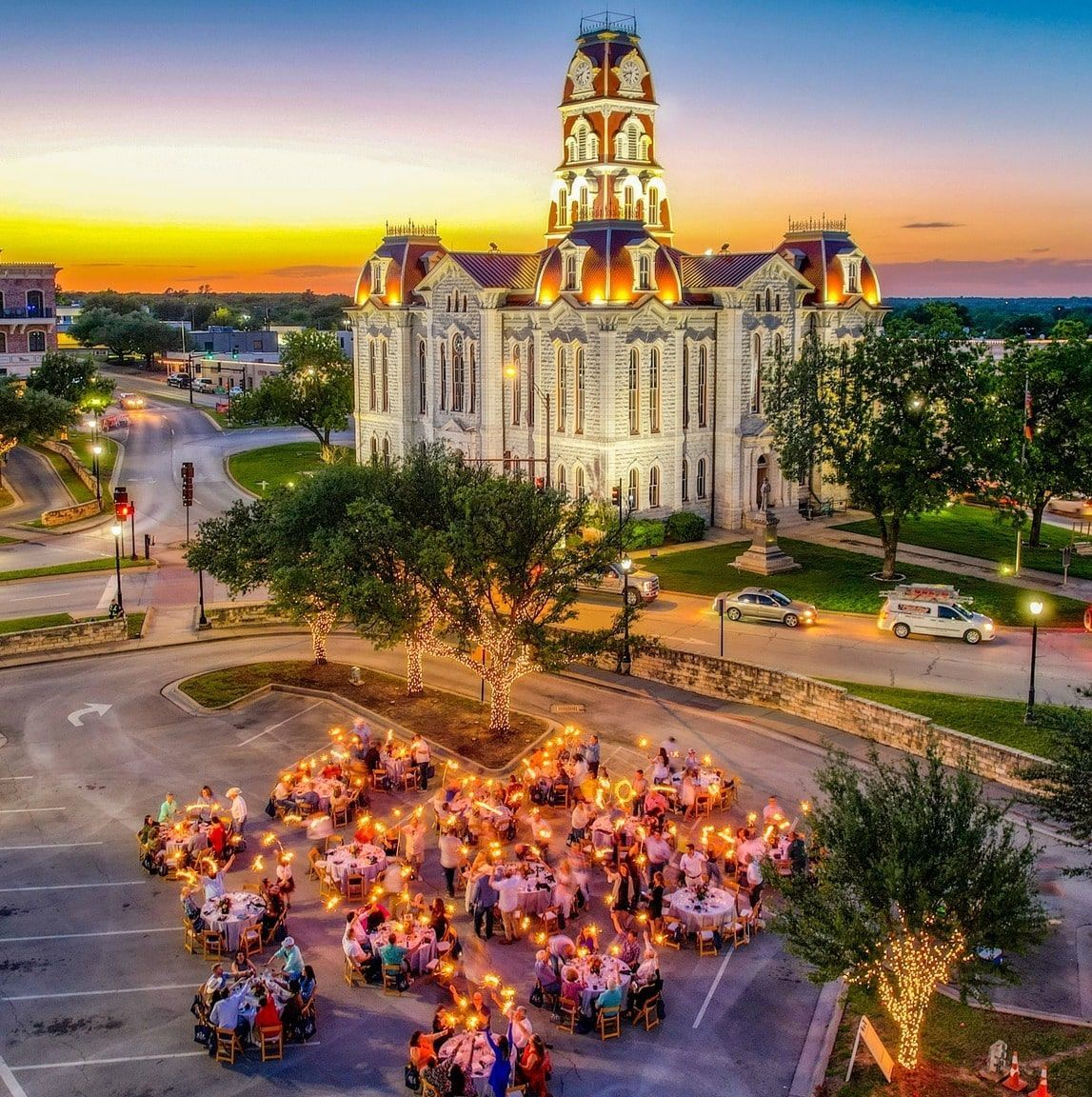 Outdoor dinner gathering in front of a historic courthouse at sunset. Tables are lit, people are dining.