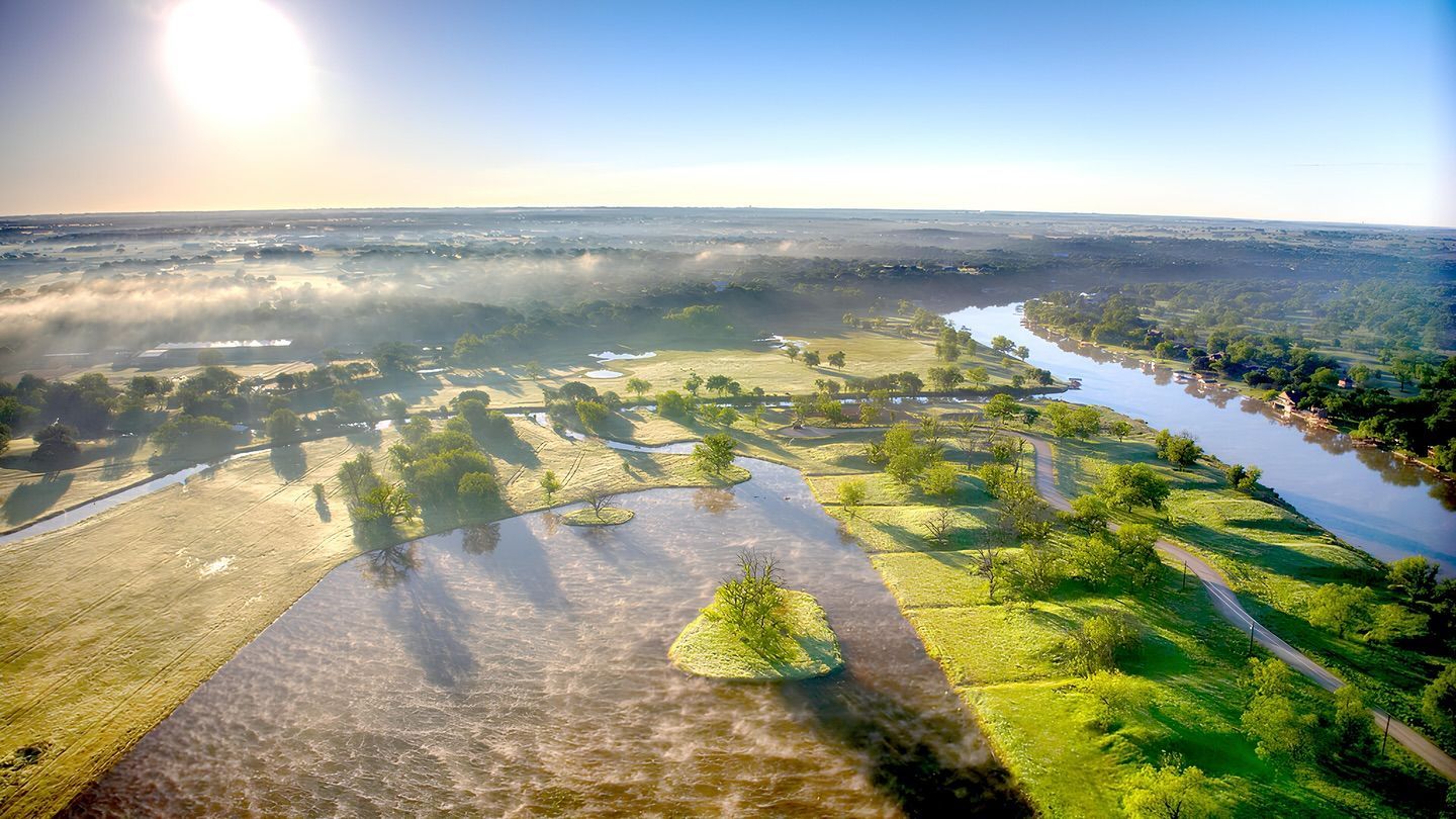Aerial view of a river flowing through a green landscape with trees, small islands, and a bright sunny sky.