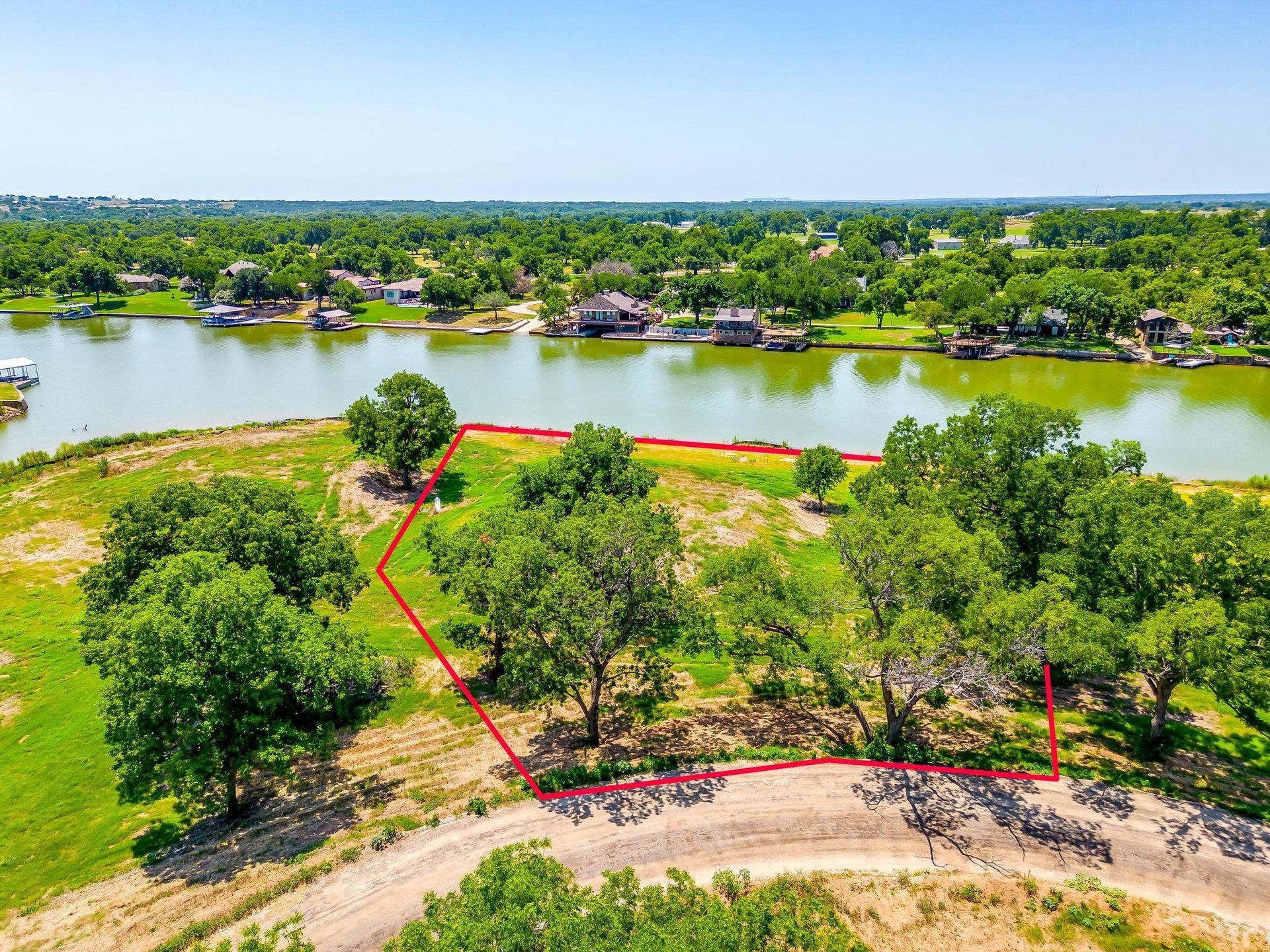 Aerial view of a lot with a red outline near a river. Green grass and trees surround the property.