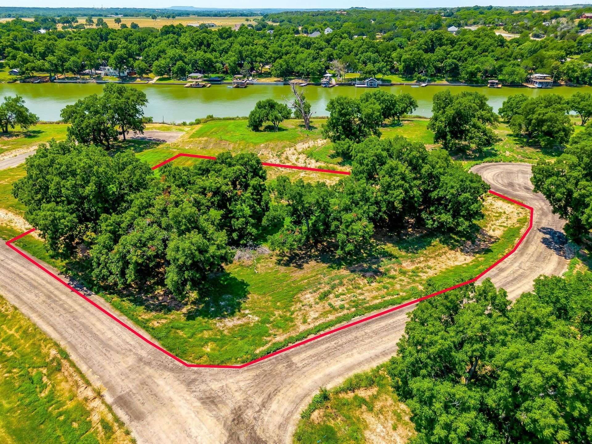 Aerial view of vacant land marked with red lines, near a river with trees.