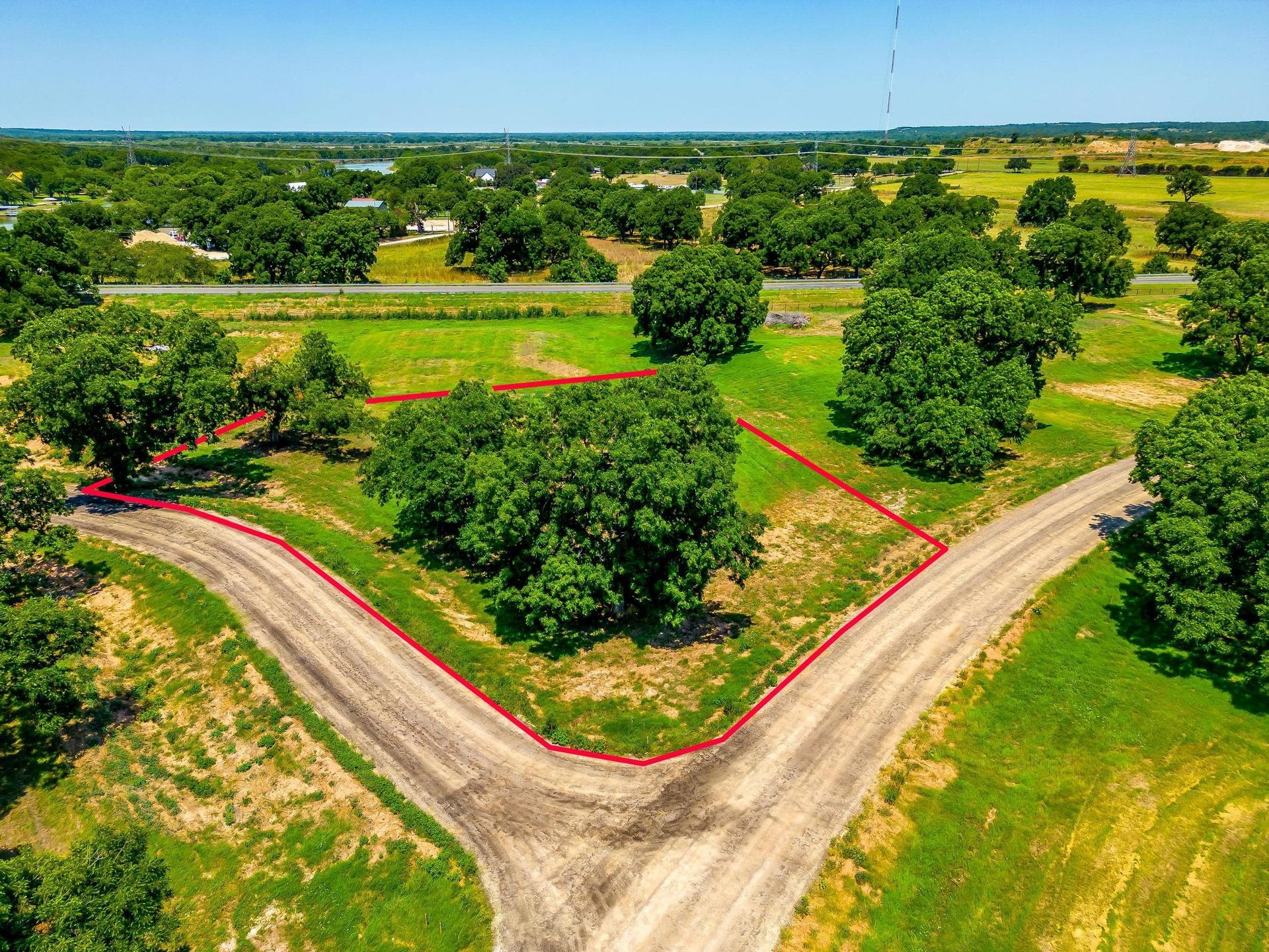 Aerial view of a lot of land with a dirt road and mature trees.