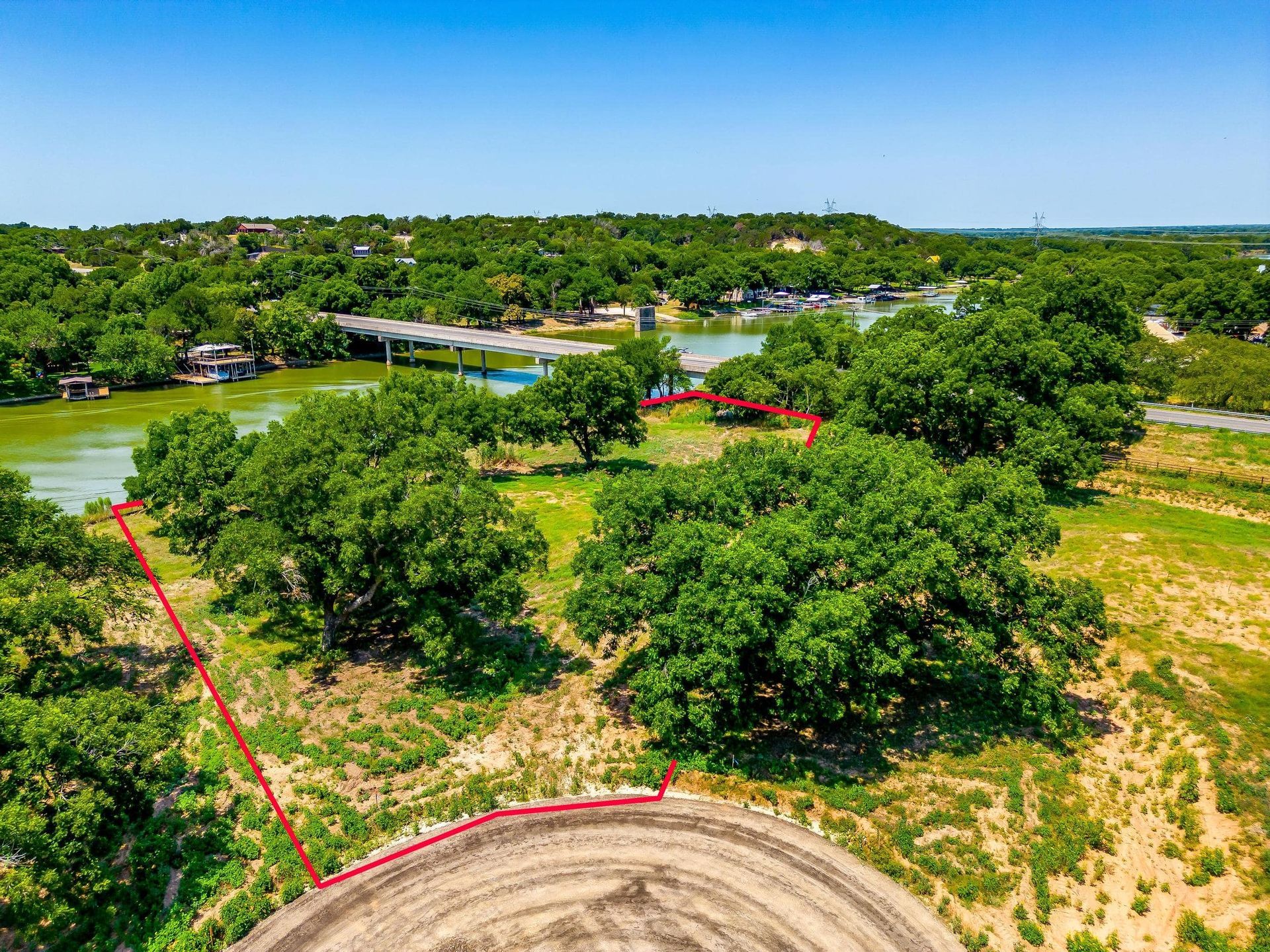 Aerial view of a waterfront lot, outlined in red, with trees and a view of a bridge and water.