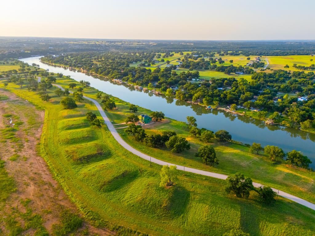 Aerial view of a river flowing through green fields and trees, with a road along the bank.