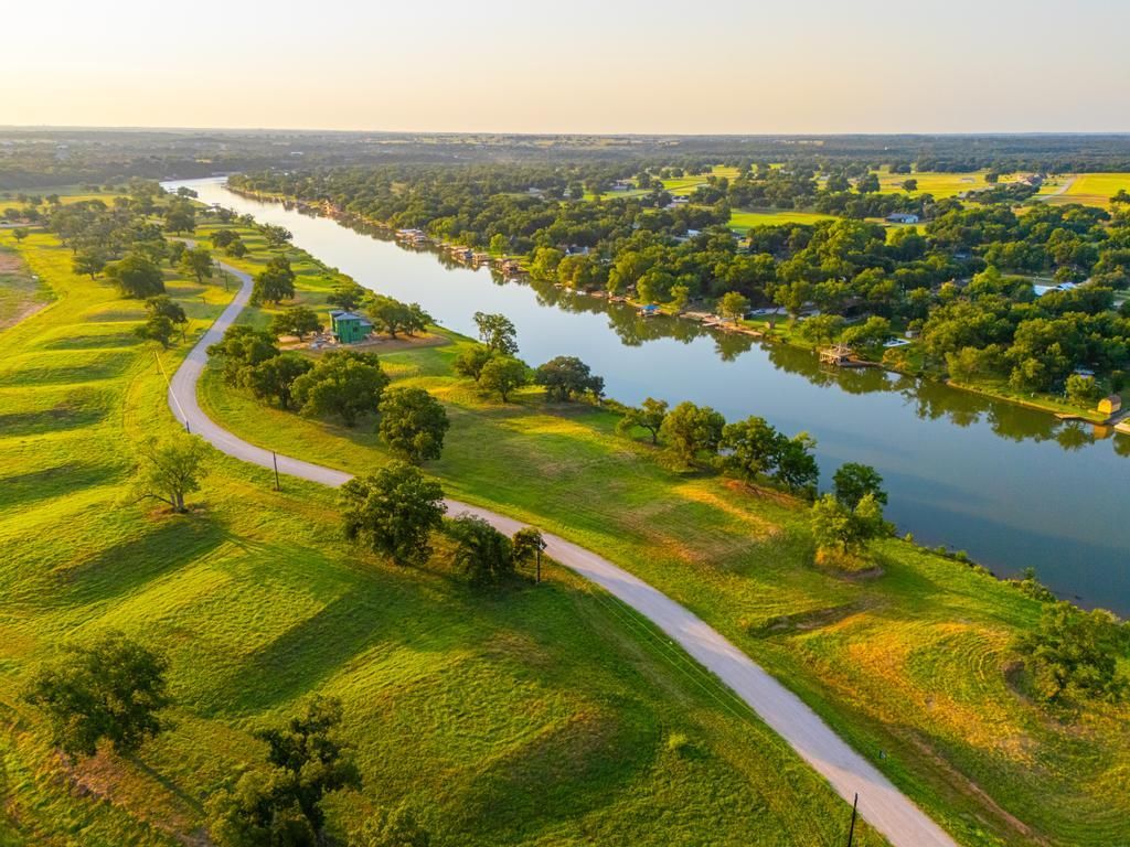A river winds through a green landscape with trees, a path, and houses; sunset light.