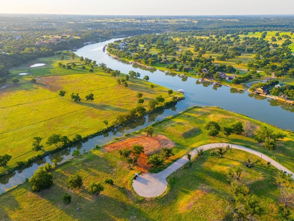 Aerial view of a river winding through green fields and scattered trees; sunny day.