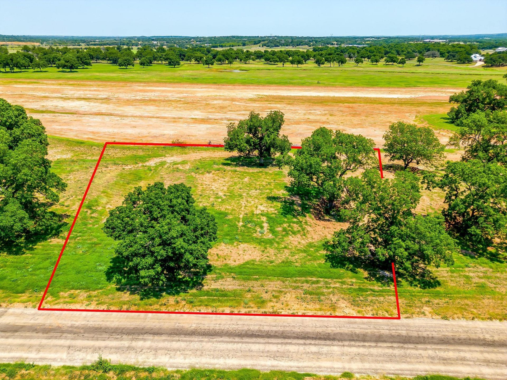 Land lot with a red outline, trees, and a dirt road. Green and brown fields in background.