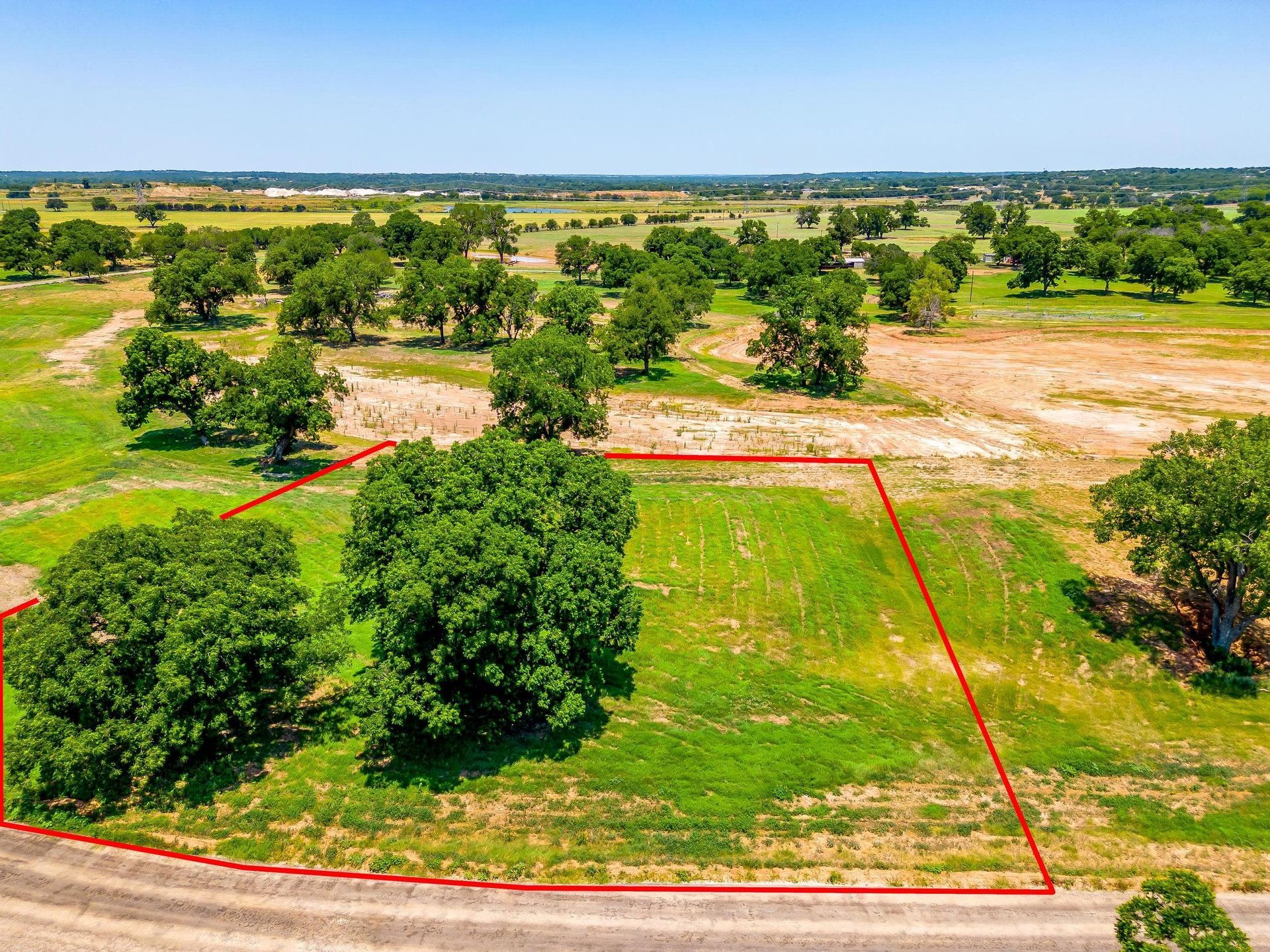 Aerial view of vacant land, outlined in red, with trees and green grass.