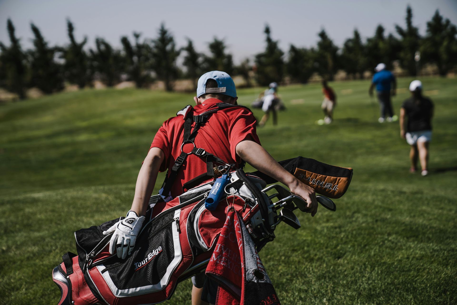 Man with golf bag on course, other golfers in the background.