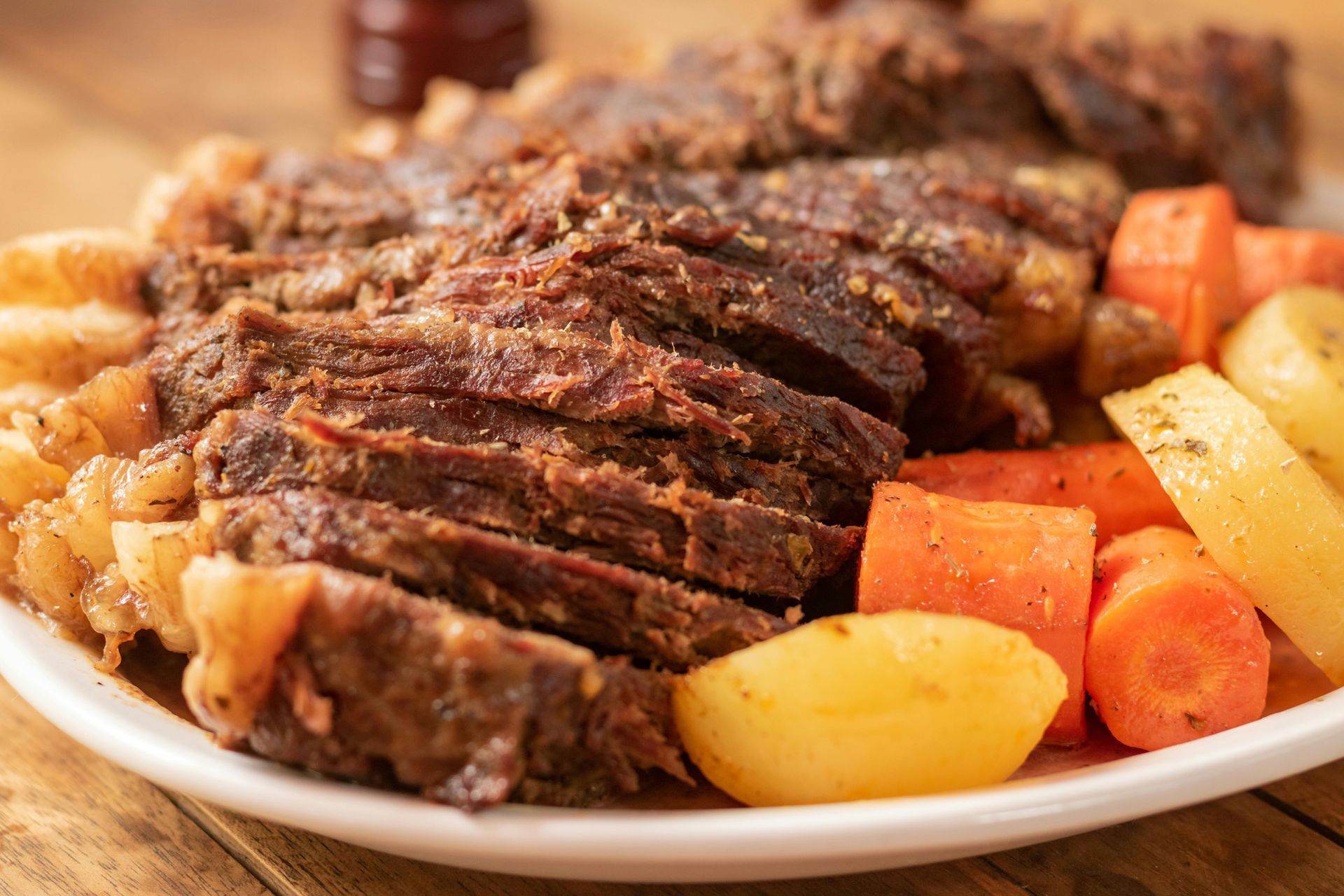 Sliced roast beef with carrots, potatoes, and gravy on a white plate.