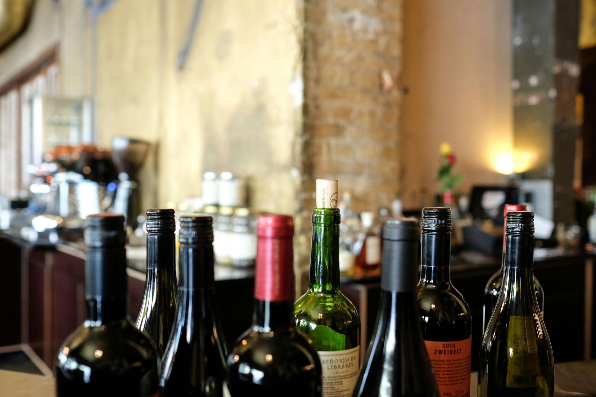 Wine bottles on a bar, some open, various colors. Interior setting with blurred background.