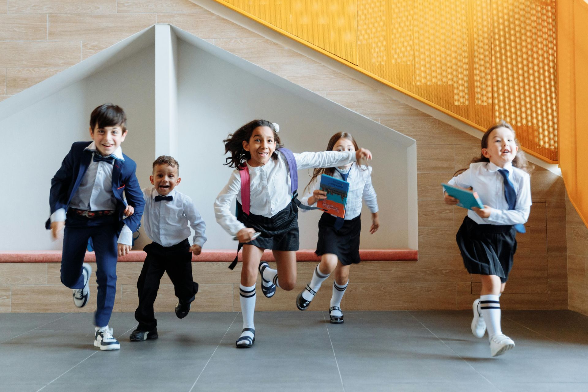 Children in uniform running joyfully in a school hallway with stairs.
