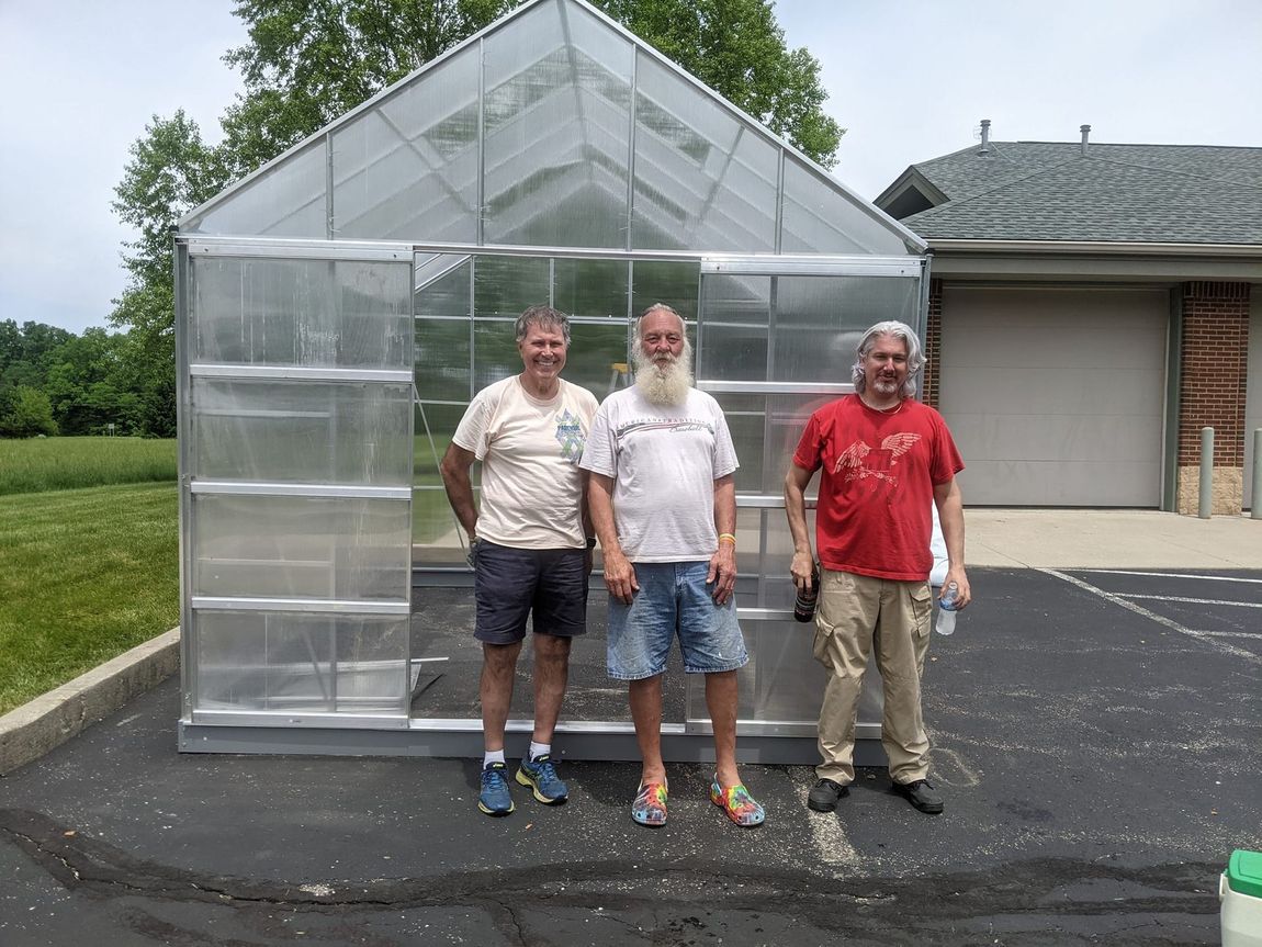 Three men standing in front of a greenhouse in a parking lot