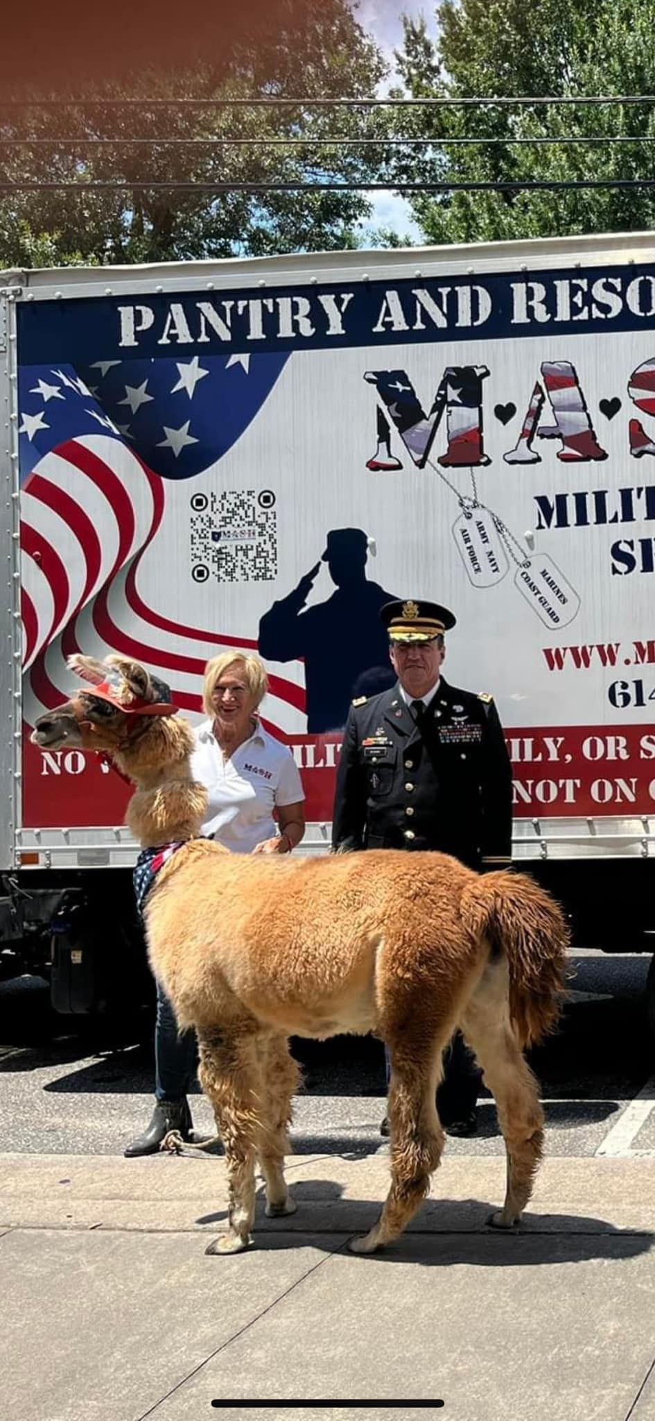 A man and a llama are standing in front of a pantry and rescue truck.